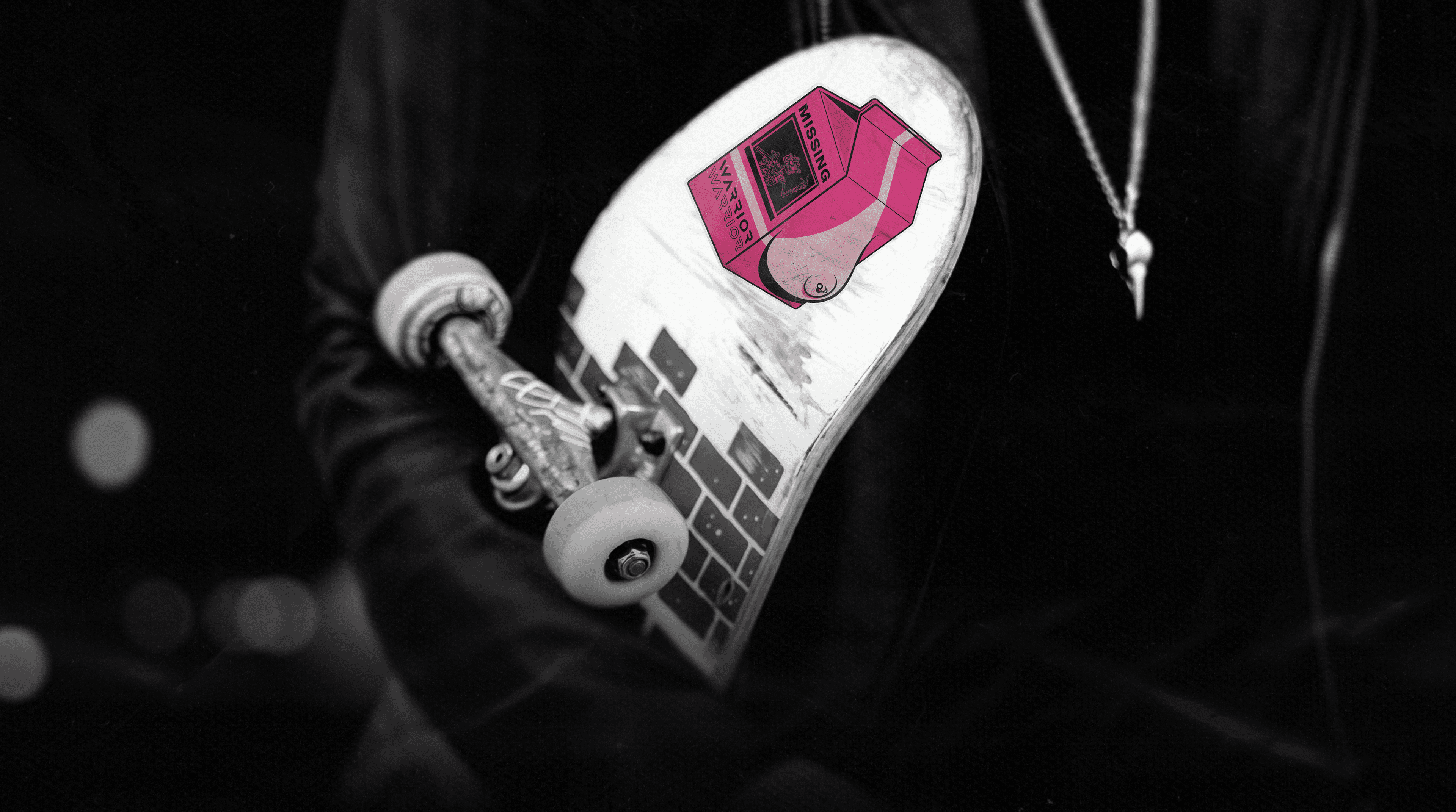 A skateboard deck covered in stickers, held under one arm