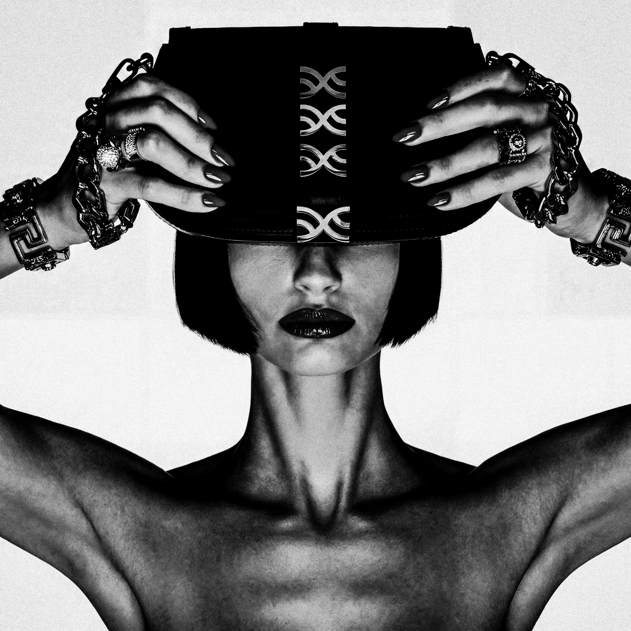 Hands in rings and chains gripping an LXIX bag, the symbol engraved in metal