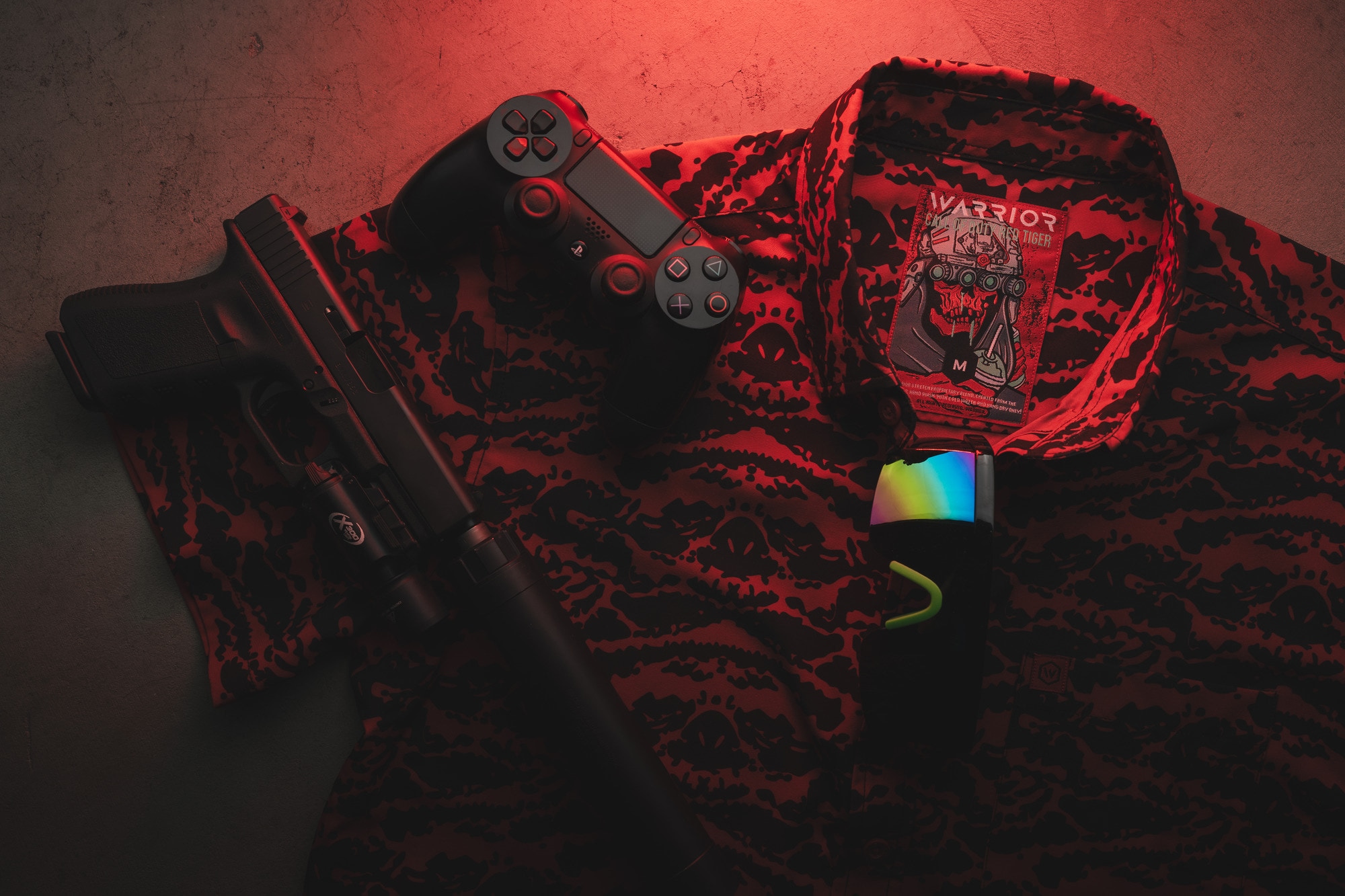 A pistol and game controller on a camo-print WARRIOR jacket, lit in red