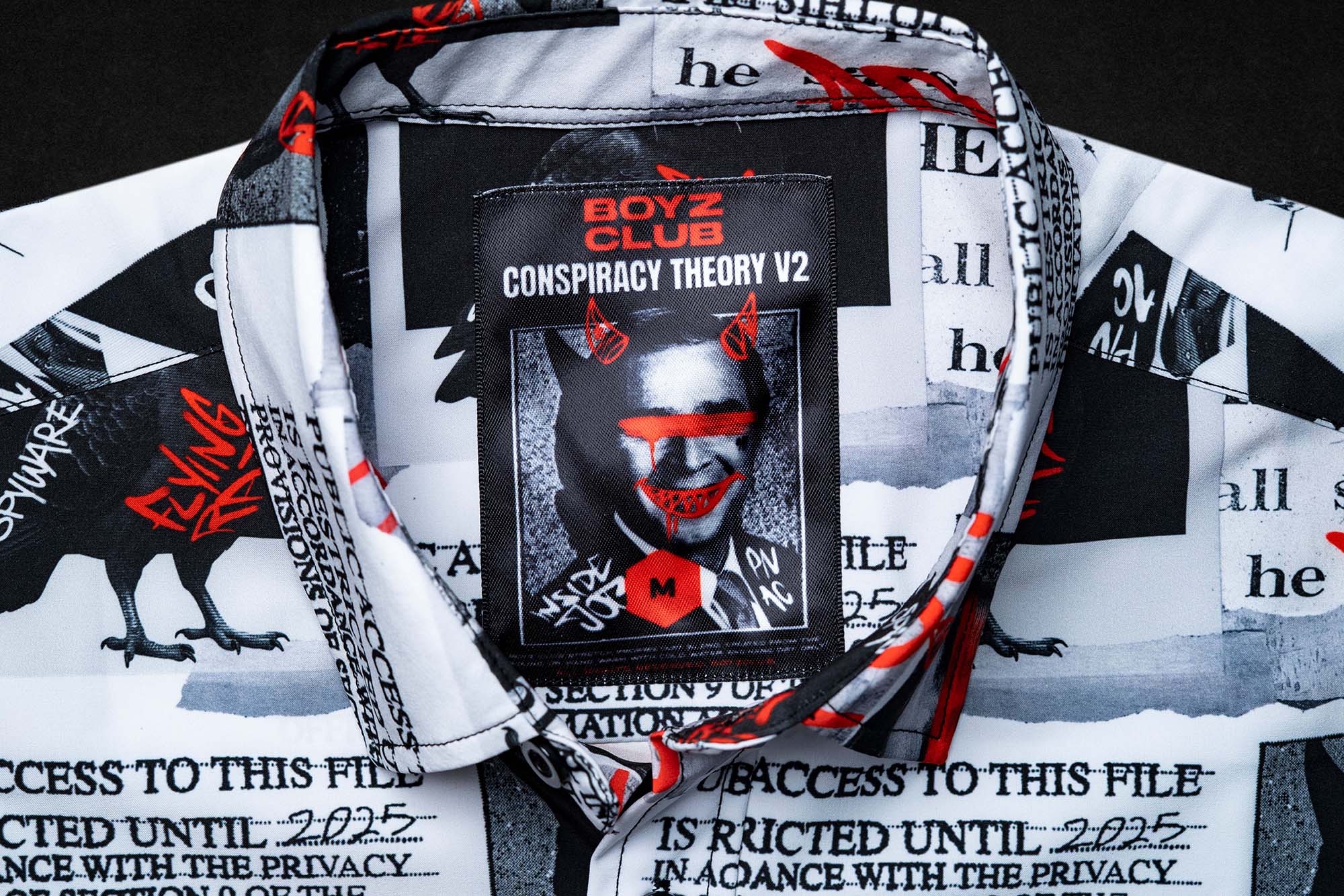 Conspiracy Theory V2 tag sewn into a newsprint-pattern garment collar